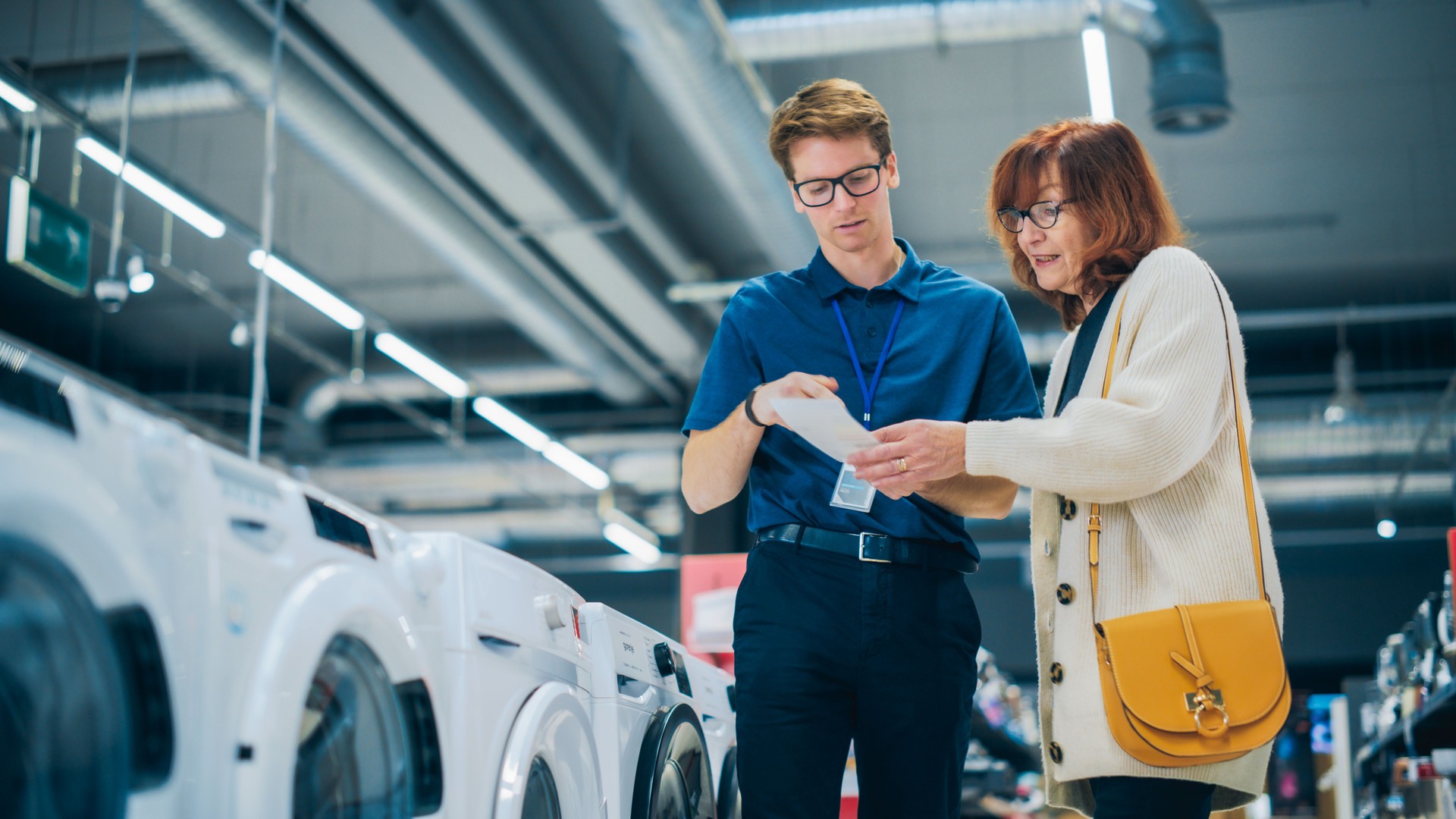 Portrait of a Senior Female Customer Seeking Expert Advice from Retail Home Electronics Expert for Washing Machine Purchase. Woman Explores Contemporary Laundry Appliance Options in a Department Store